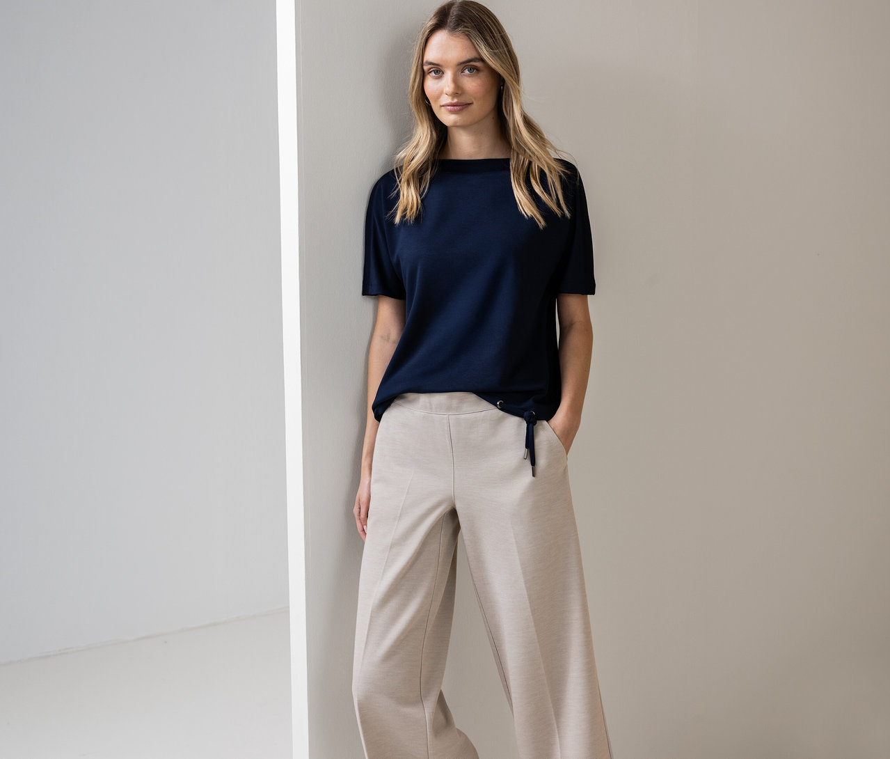 Kobieta pozuje w granatowej koszulce Street One i beżowych spodniach przy ścianie.