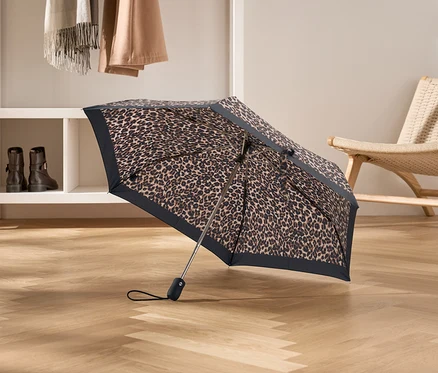 Otwarty parasol w lamparcie cętki stoi na drewnianej podłodze.