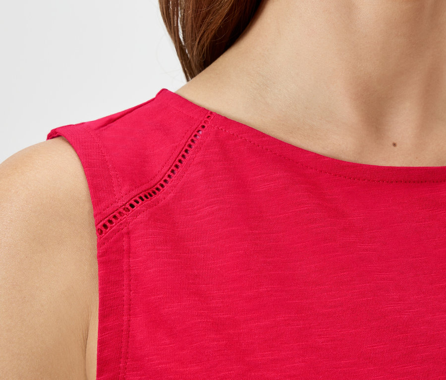 Zbliżenie kobiety ubranej w czerwoną bluzkę bez rękawów z dziurkowanym wzorem na ramionach.