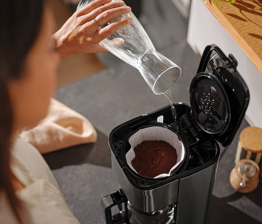 Kobieta nalewa wodę ze szklanej karafki do ekspresu do kawy.