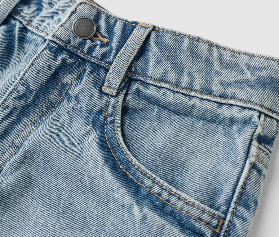 Zbliżenie jasnoniebieskich dżinsów z guzikiem i kieszenią.