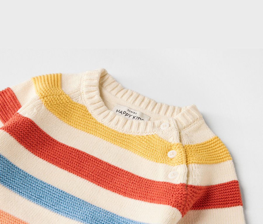 Zbliżenie na rozpinany sweter dziecięcy w paski w kolorach czerwonym, żółtym i niebieskim, zapinany na białe guziki.