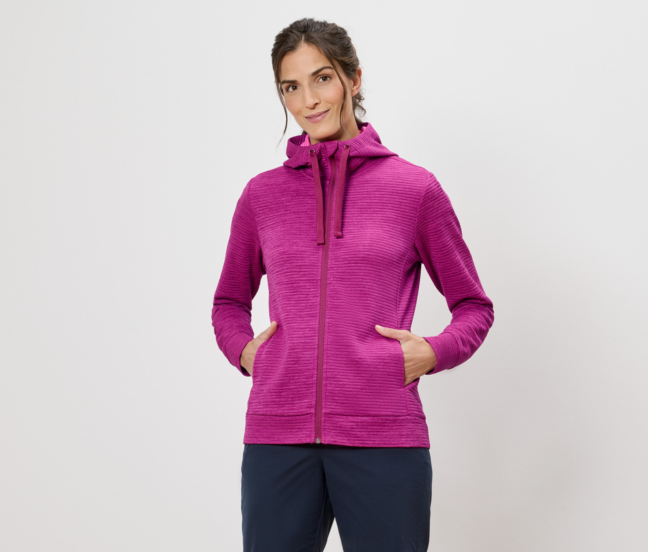 Kobieta w różowej bluzie z kapturem z rękami w kieszeniach na białym tle.