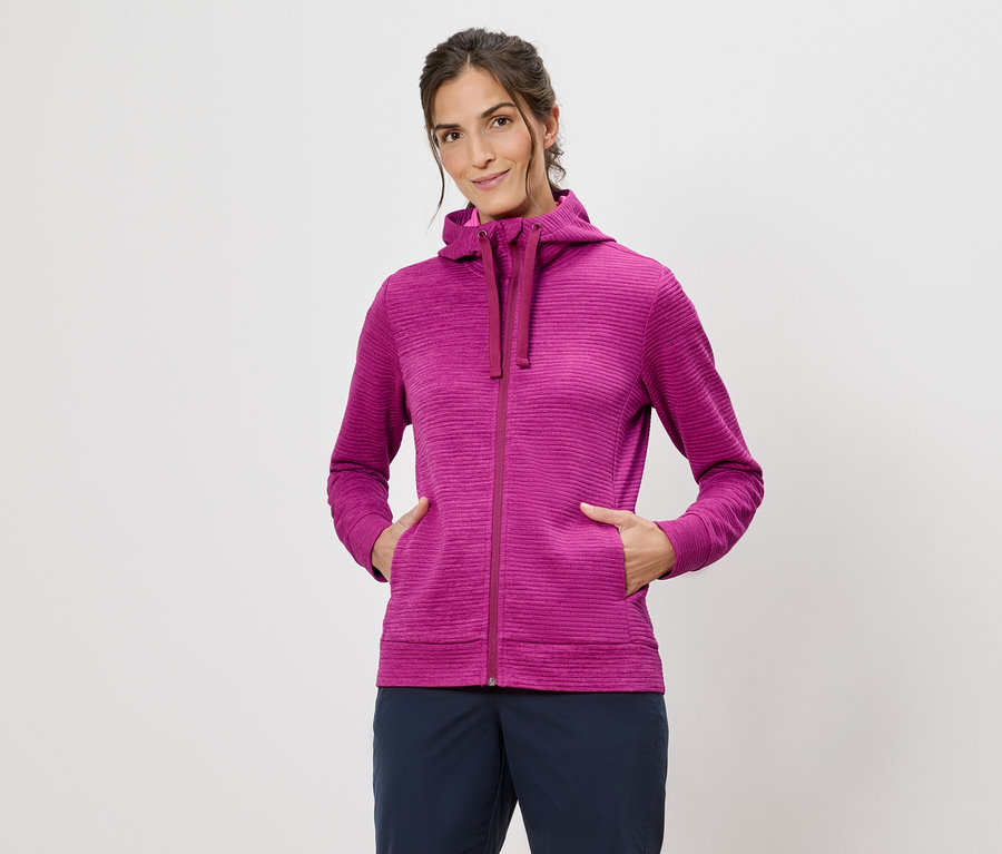 Kobieta w różowej bluzie z kapturem z rękami w kieszeniach na białym tle.