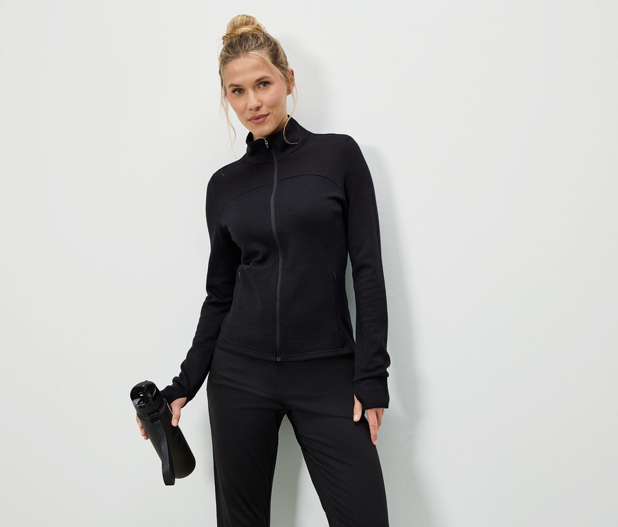 Kobieta w czarnej kurtce i spodniach trzyma czarną butelkę na wodę na białym tle.