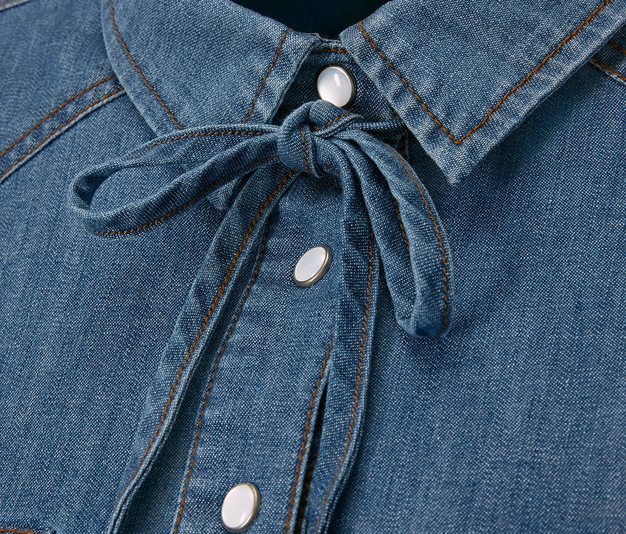 Zbliżenie na dżinsową koszulę z guzikami i wiązanym dekoltem.