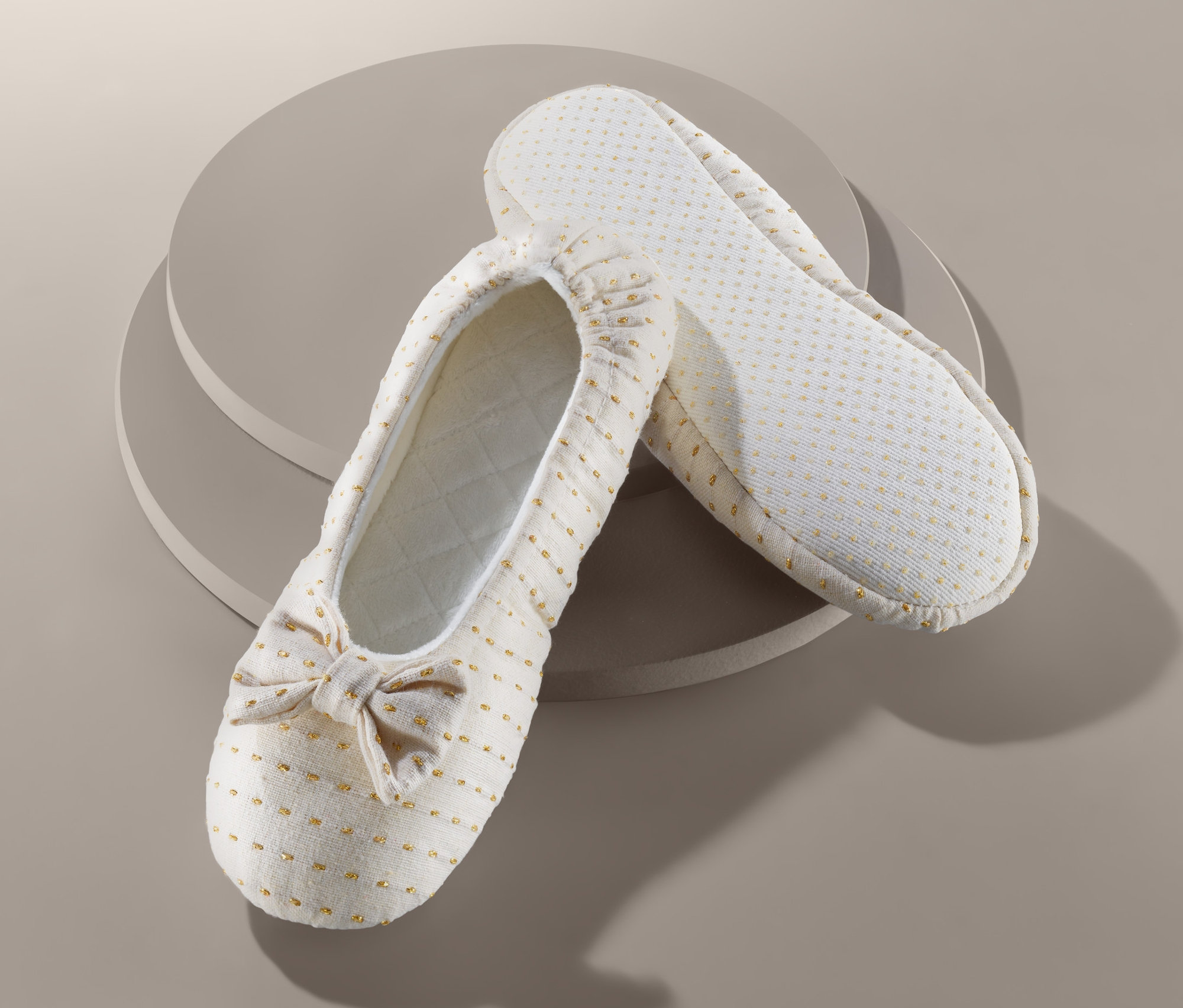 Dwa kapcie baleriny leżą na sobie na beżowym tle.