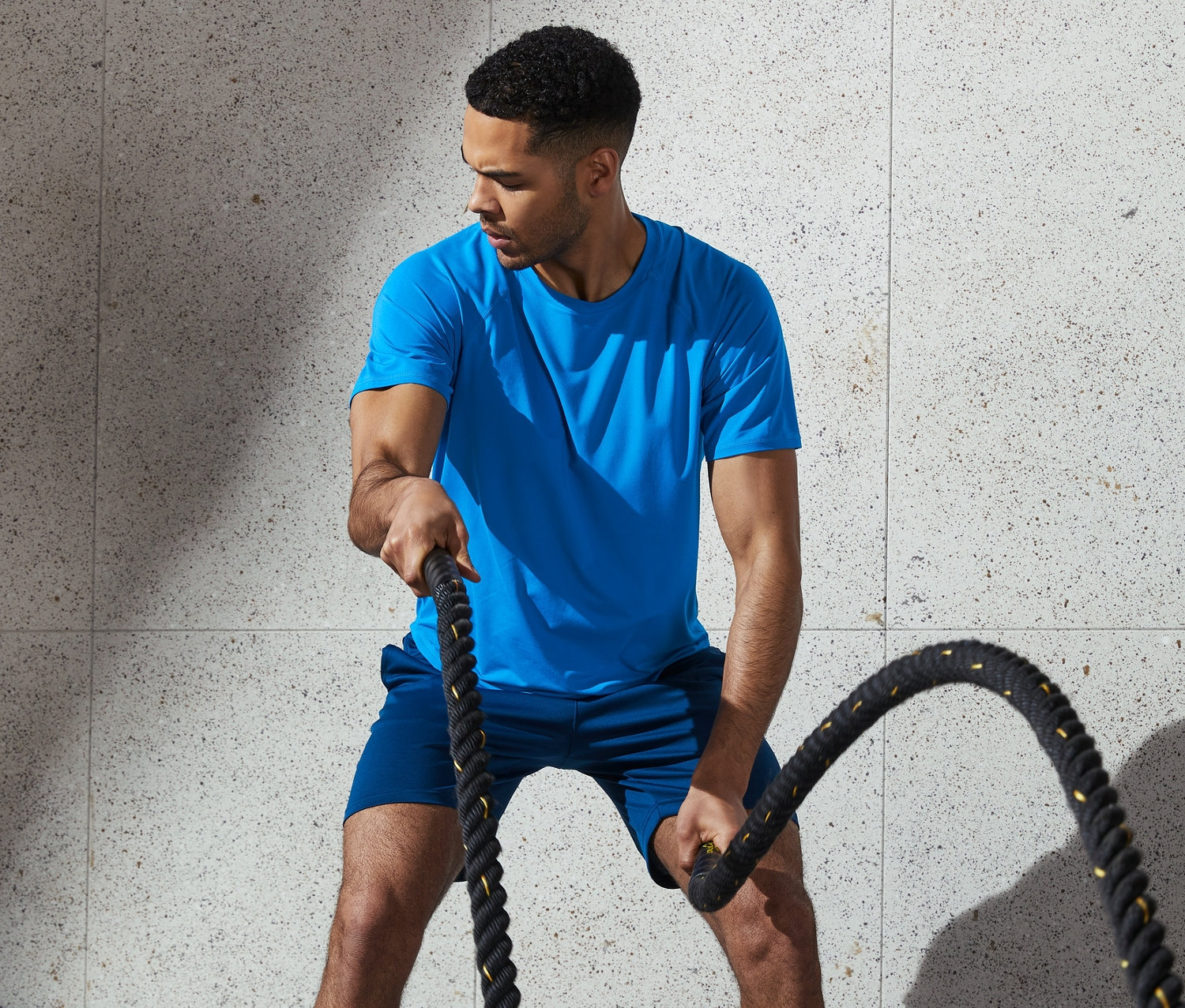 Mężczyzna ćwiczy z linami w niebieskiej koszulce funkcyjnej.