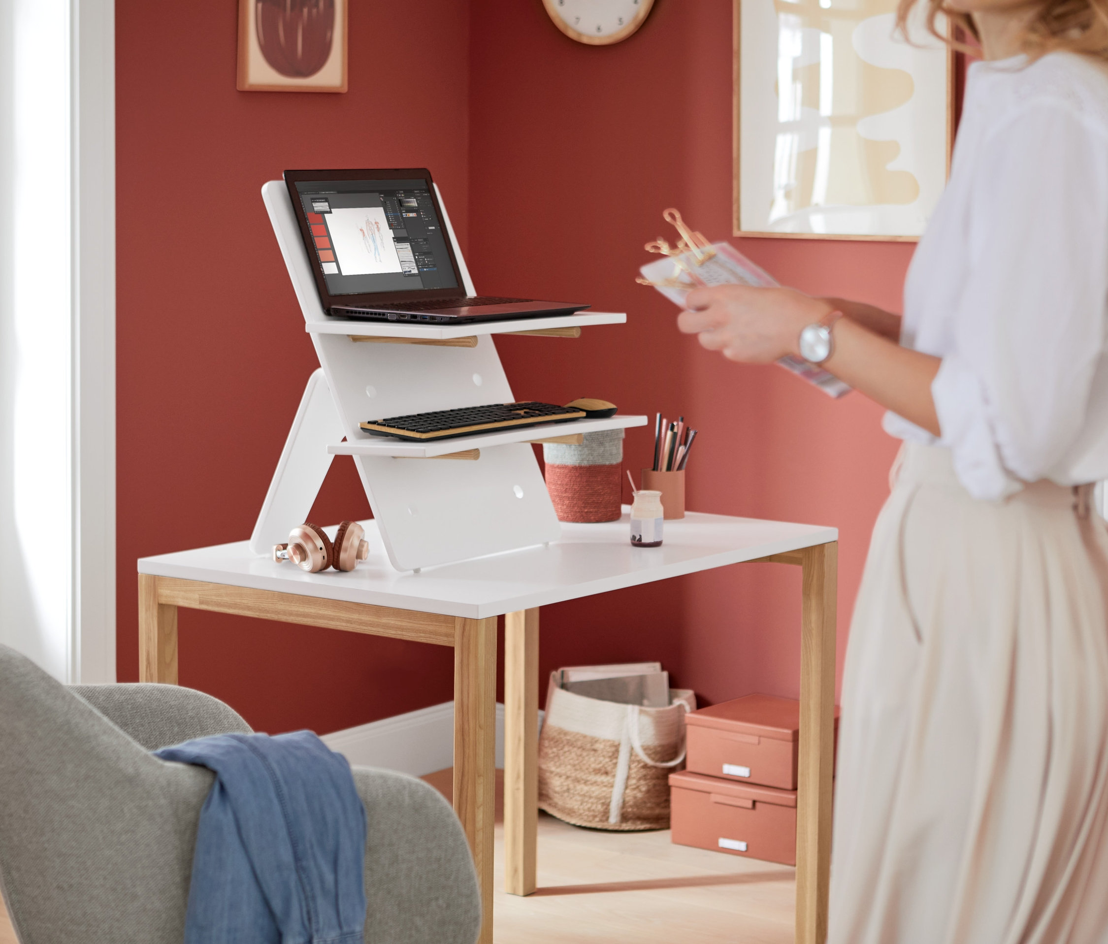 Kobieta stoi obok białego biurka z białą nakładką na biurko, na której znajduje się laptop i klawiatura.