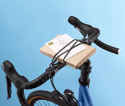 Paczka na kierownicy roweru przymocowana taśmą elastyczną na kierownicę.