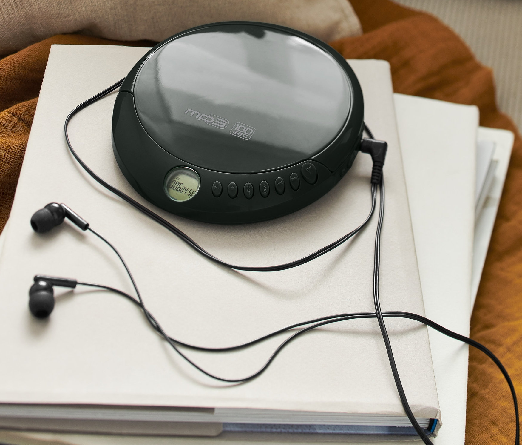 Czarny, przenośny odtwarzacz CD z czarnymi słuchawkami leży na stosie książek.