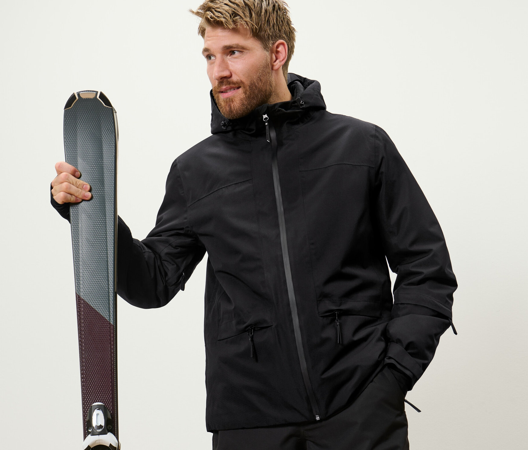 Mężczyzna trzyma narty. Ma na sobie czarną kurtkę narciarską.