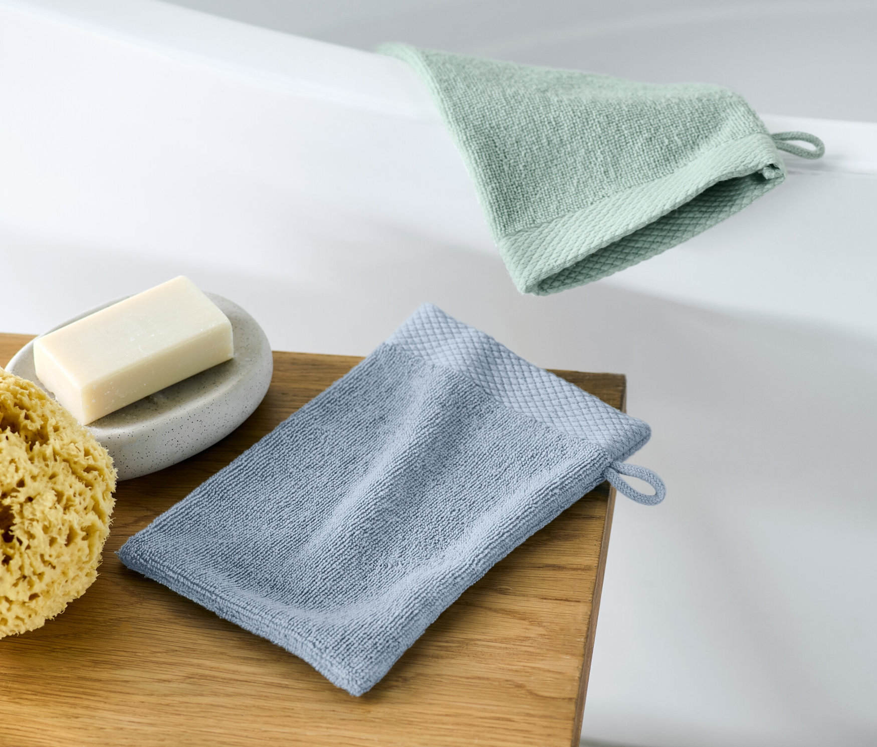 Dwie myjki do kąpieli leżą na drewnianym stołku obok mydła i gąbki.