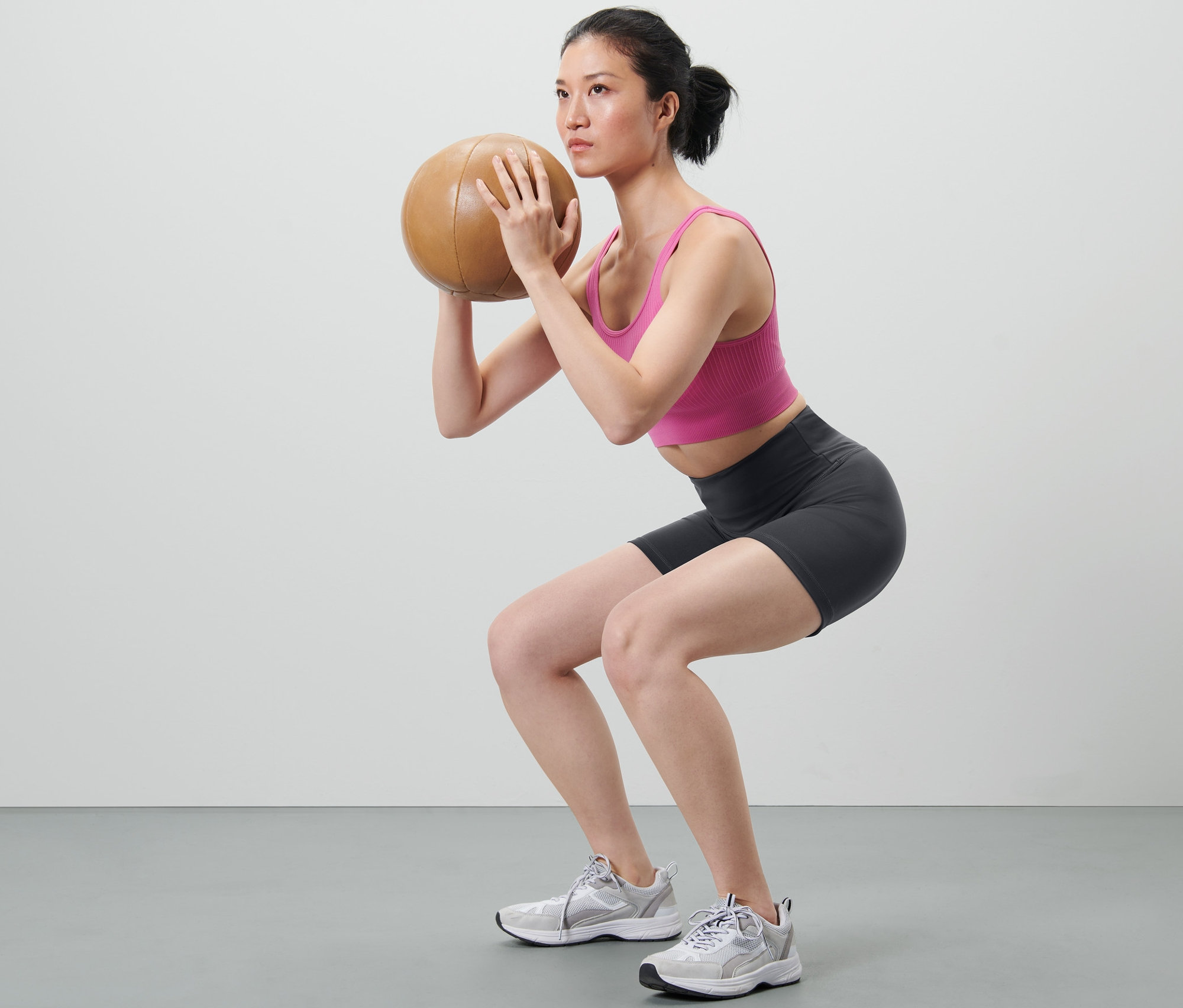 Kobieta robi przysiady z piłką sportową, ubrana w krótkie legginsy sportowe.