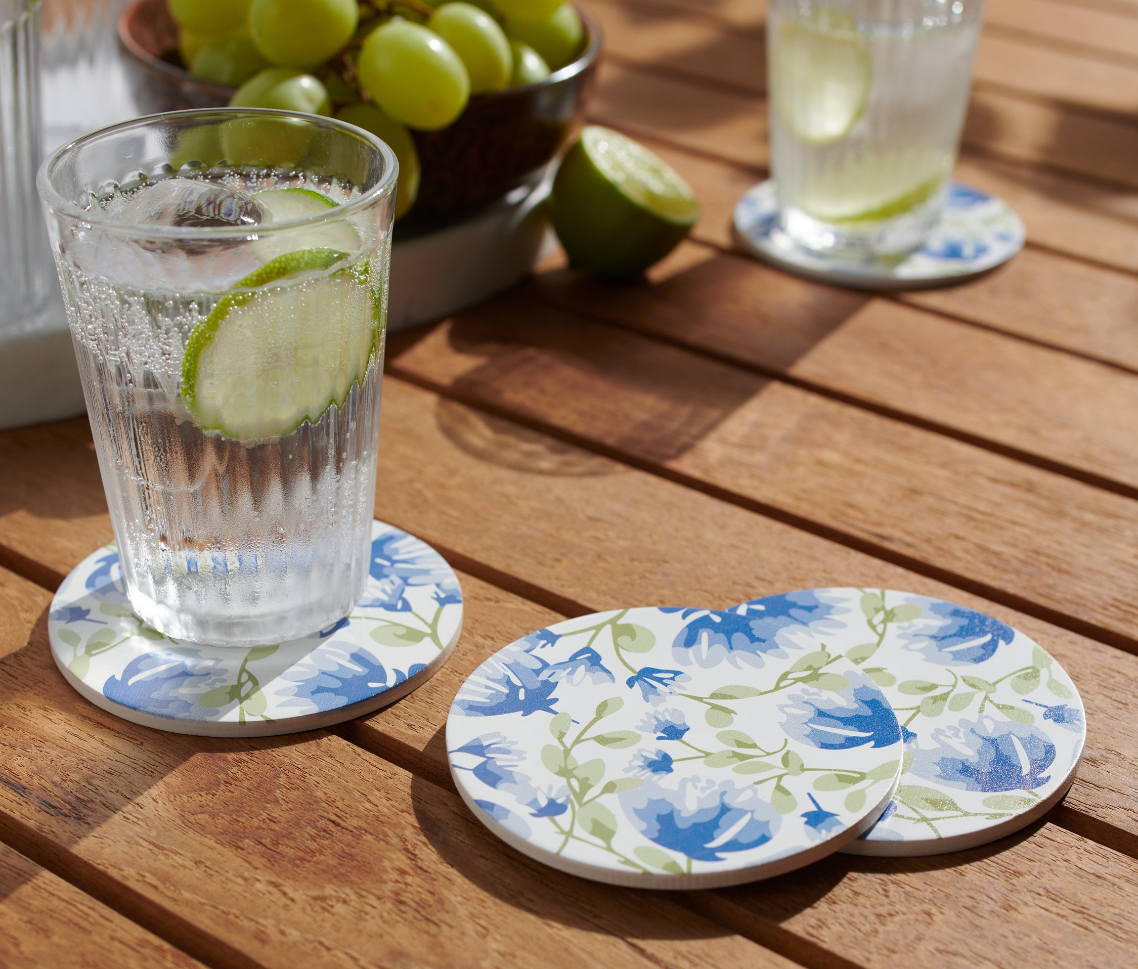 Szklanka z napojem stoi na jednej z 4 podkładek na drewnianym stole.