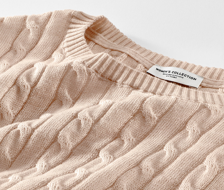 Zbliżenie na kremowy sweter z warkoczowym wzorem.