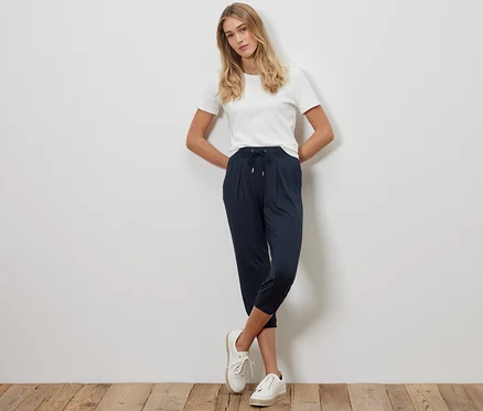 Blondwłosa kobieta pozuje w granatowych spodniach dżersejowych o długości 3/4 i białym T-shircie.