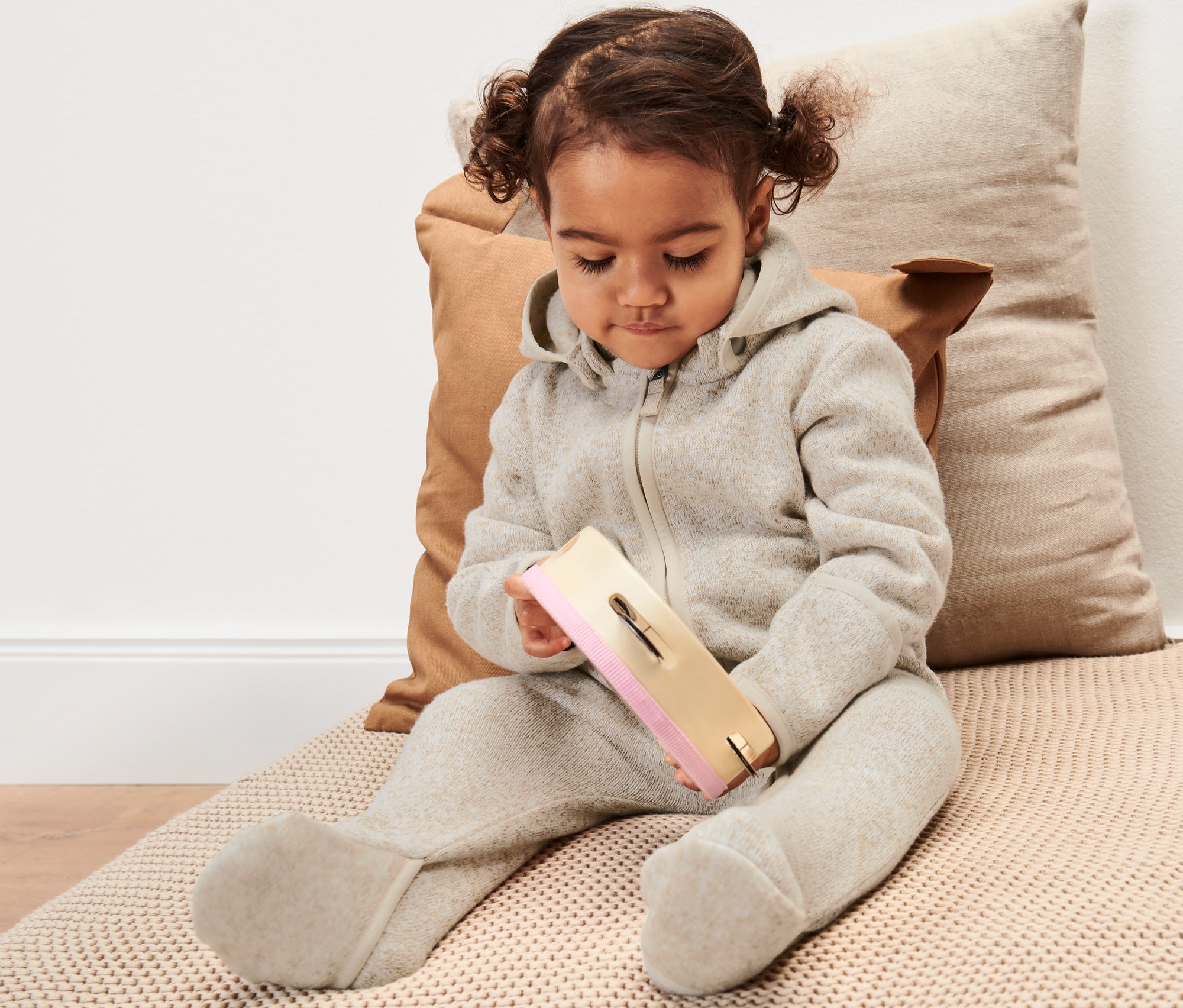 Małe dziecko siedzi i bawi się zabawką, ubrane w dzianinowy kombinezon niemowlęcy.