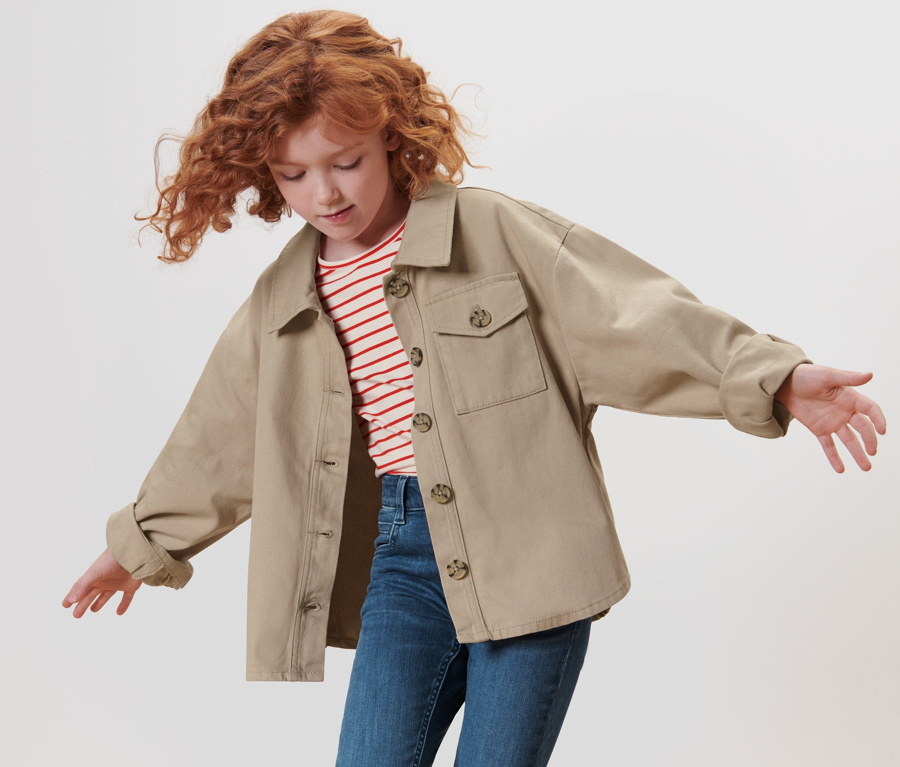 Ruda, kręcona dziewczyna macha rękami, ubrana w kurtkę dżinsową.