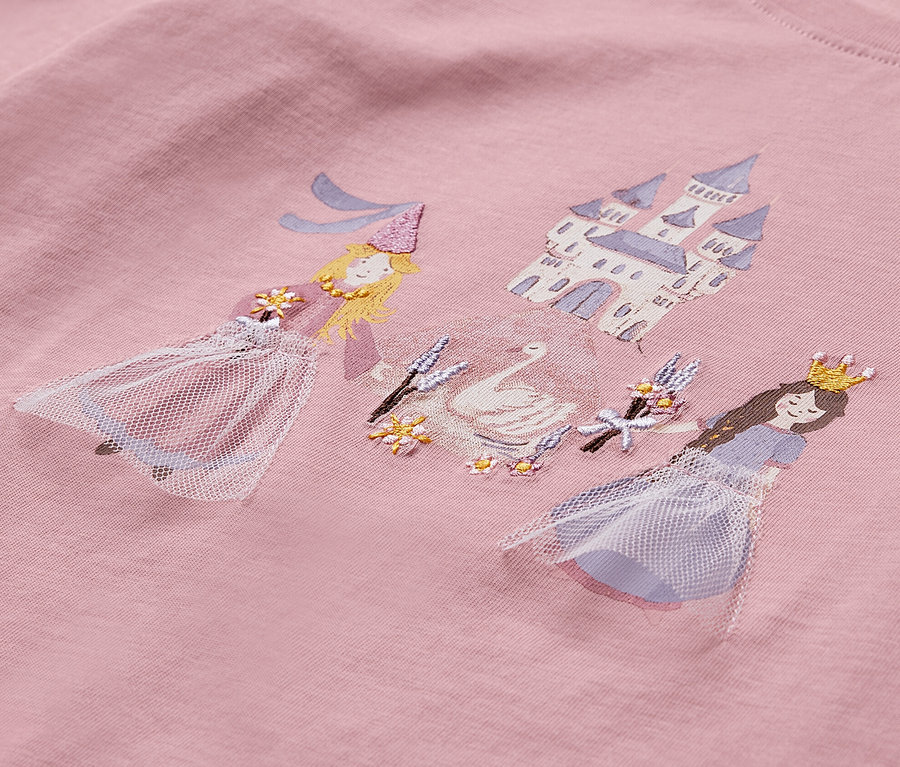Zbliżenie na różową koszulkę z długim rękawem z nadrukiem dwóch księżniczek, łabędzia i zamku.