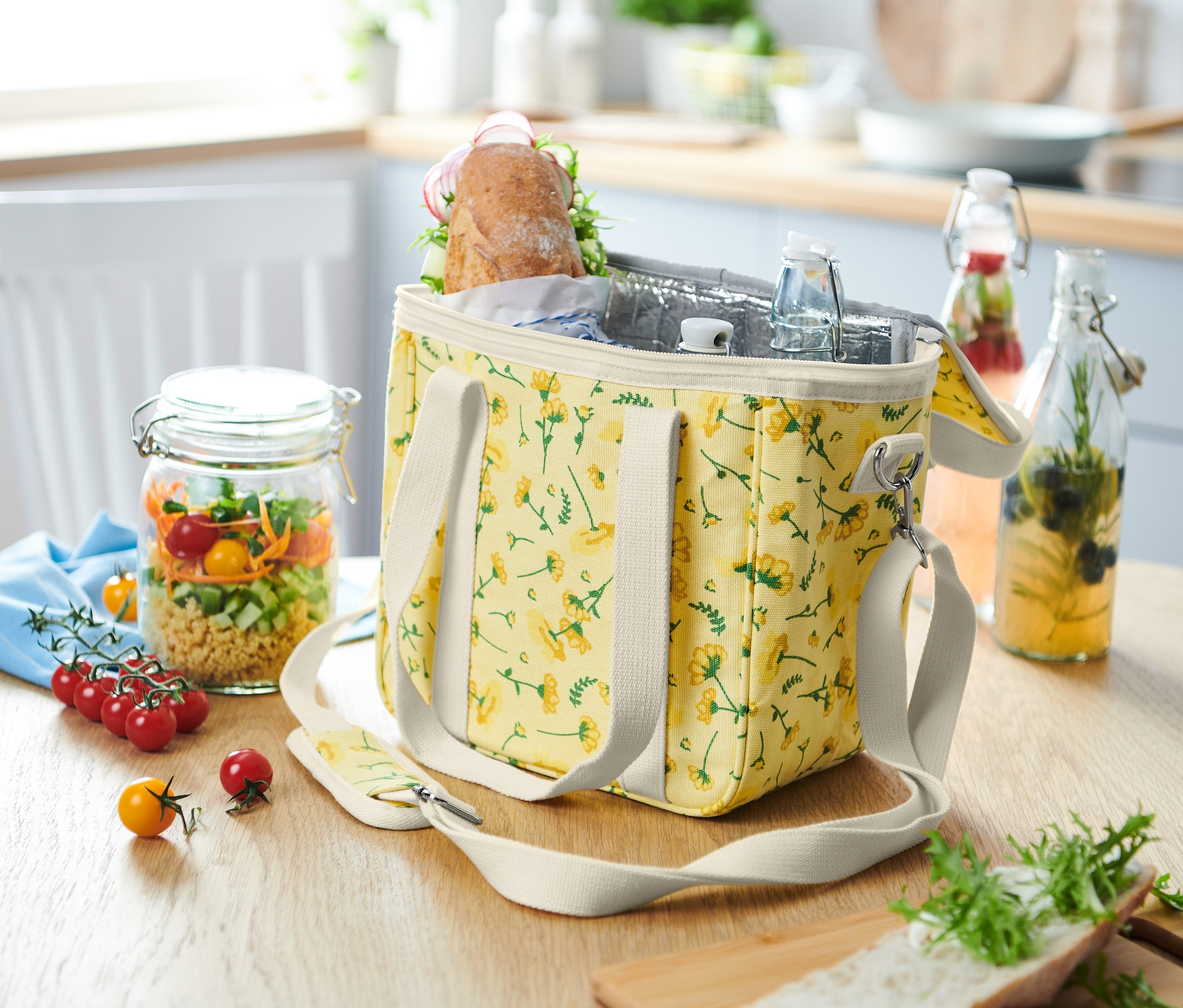 Torba termoizolacyjna w kwiaty stoi na stole obok słoika z sałatką.