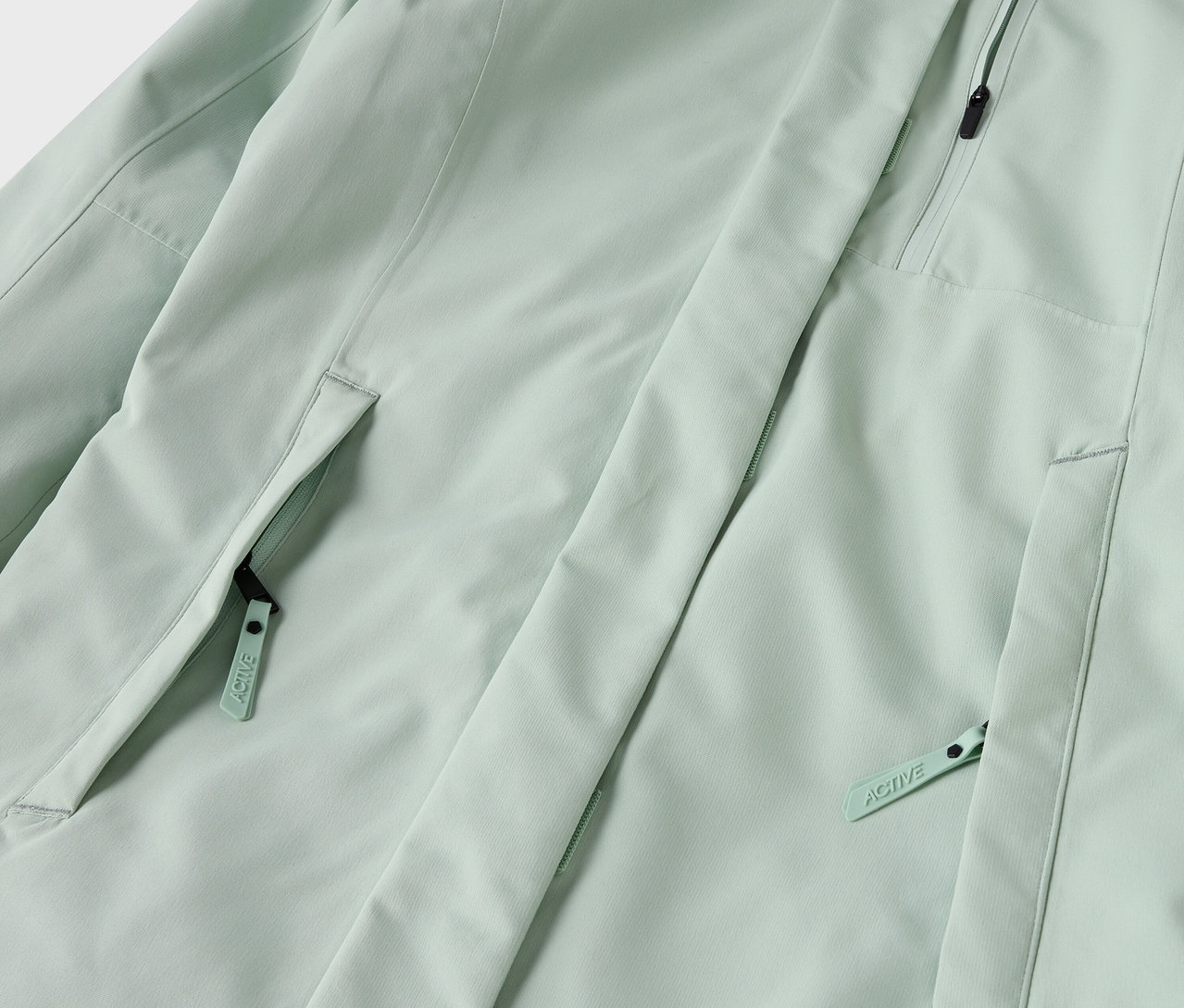 Szczegół jasnozielonej kurtki z kieszeniami zapinanymi na zamek.