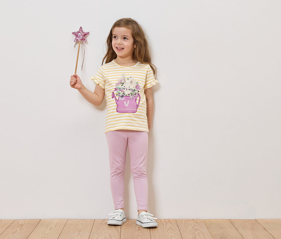Dziewczynka trzyma różdżkę z gwiazdą, ma na sobie koszulkę w paski z konewką i kwiatami oraz różowe legginsy.