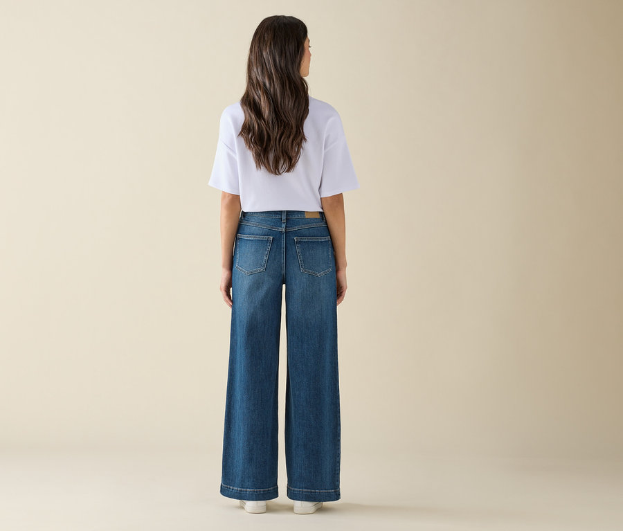 Kobieta stoi tyłem do aparatu, ma na sobie szerokie dżinsy i białą koszulkę.