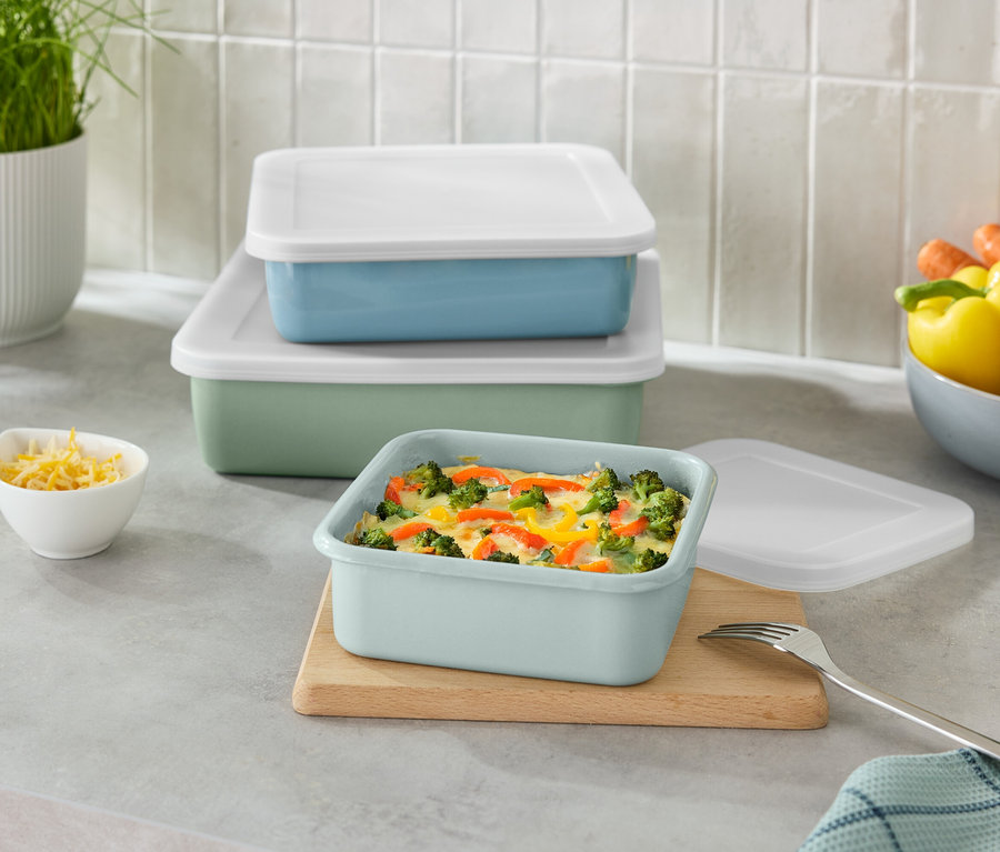 Ułożone w stos zielone i niebieskie prostokątne pojemniki z białymi pokrywkami oraz mała miseczka z tartym serem.