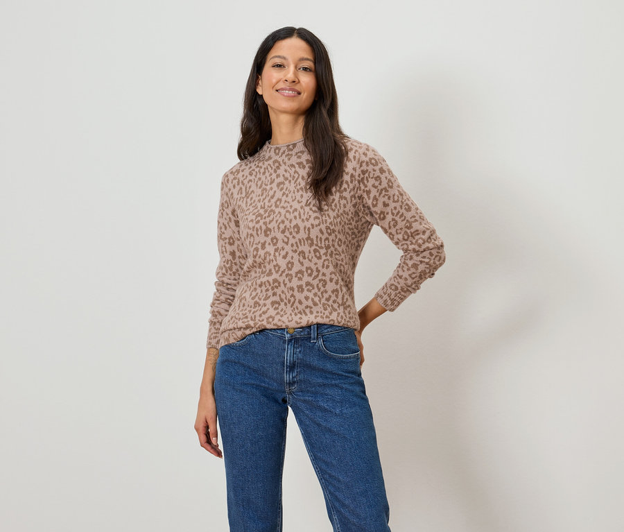 Kobieta ma na sobie jasnobrązowy sweter w panterkę i niebieskie dżinsy.