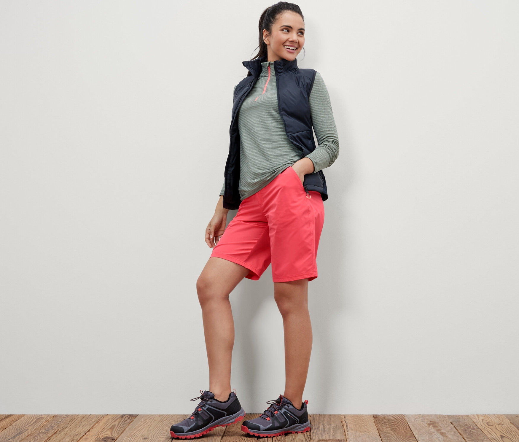 Kobieta stoi z rękami w kieszeniach różowych szortów funkcyjnych z softshellu.