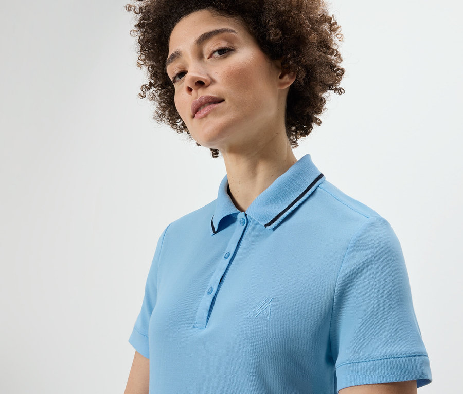 Kobieta z kręconymi włosami nosi jasnoniebieską funkcyjną koszulkę polo.