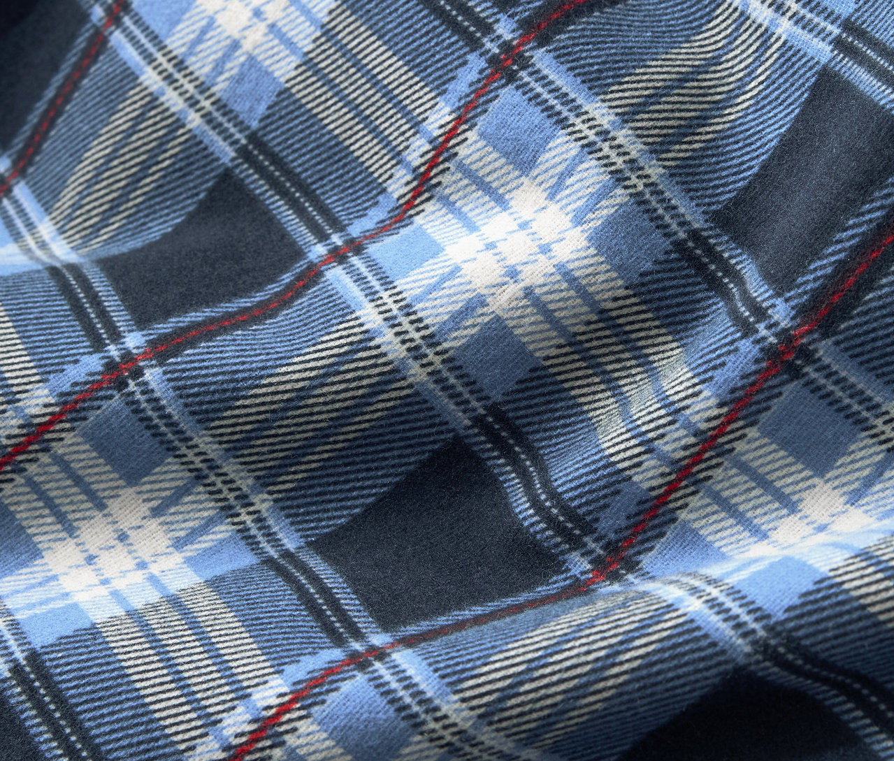 Szczegółowe ujęcie tkaniny w niebieską kratę, uzupełnioną białymi i cienkimi czerwonymi paskami.