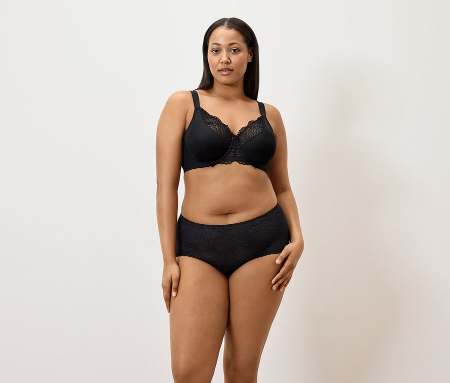 Kobieta ma na sobie czarny biustonosz minimizer i czarne figi (5 par) na białym tle.