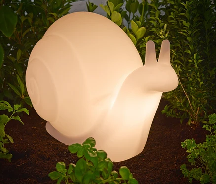 Zbliżenie lampy solarnej premium „Ślimak” stojącej na ziemi wśród roślin.
