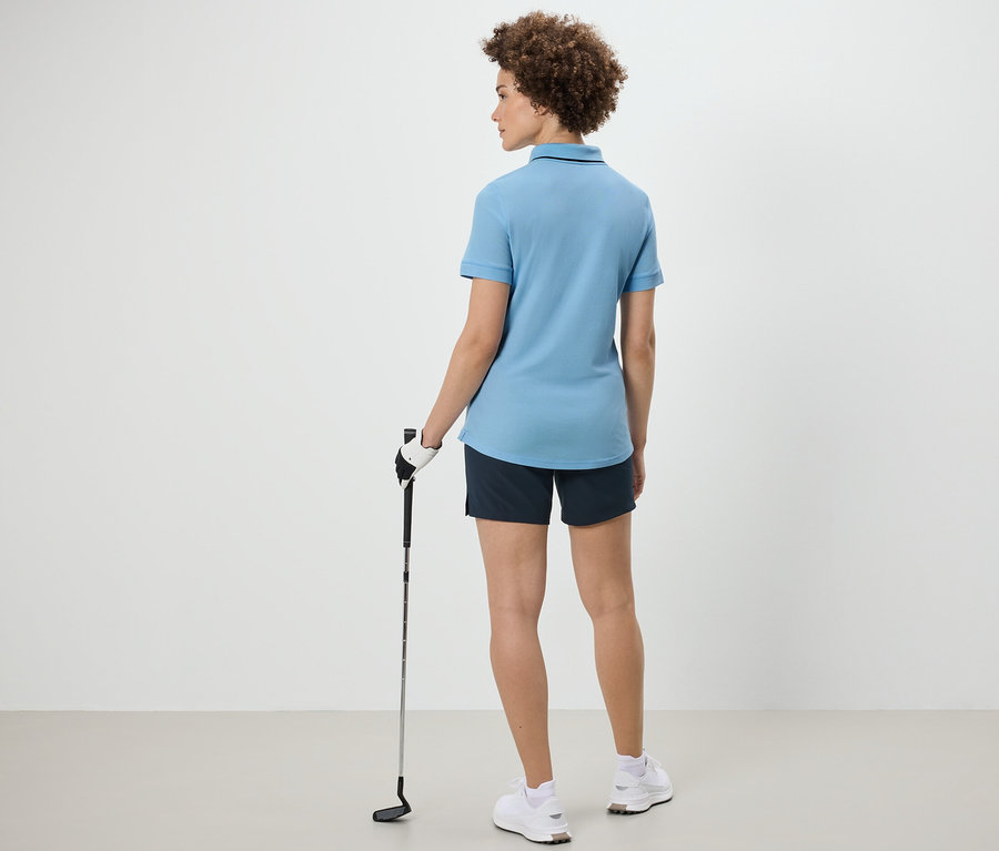 Kobieta od tyłu trzyma kij golfowy i ma na sobie jasnoniebieską funkcyjną koszulkę polo.
