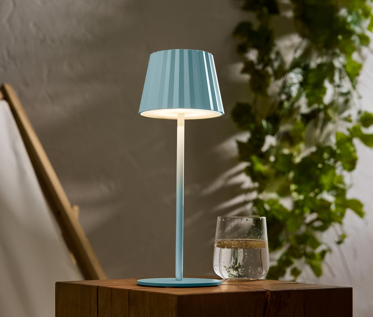 Niebieska lampa w paski stoi na drewnianym stole obok szklanki wody.