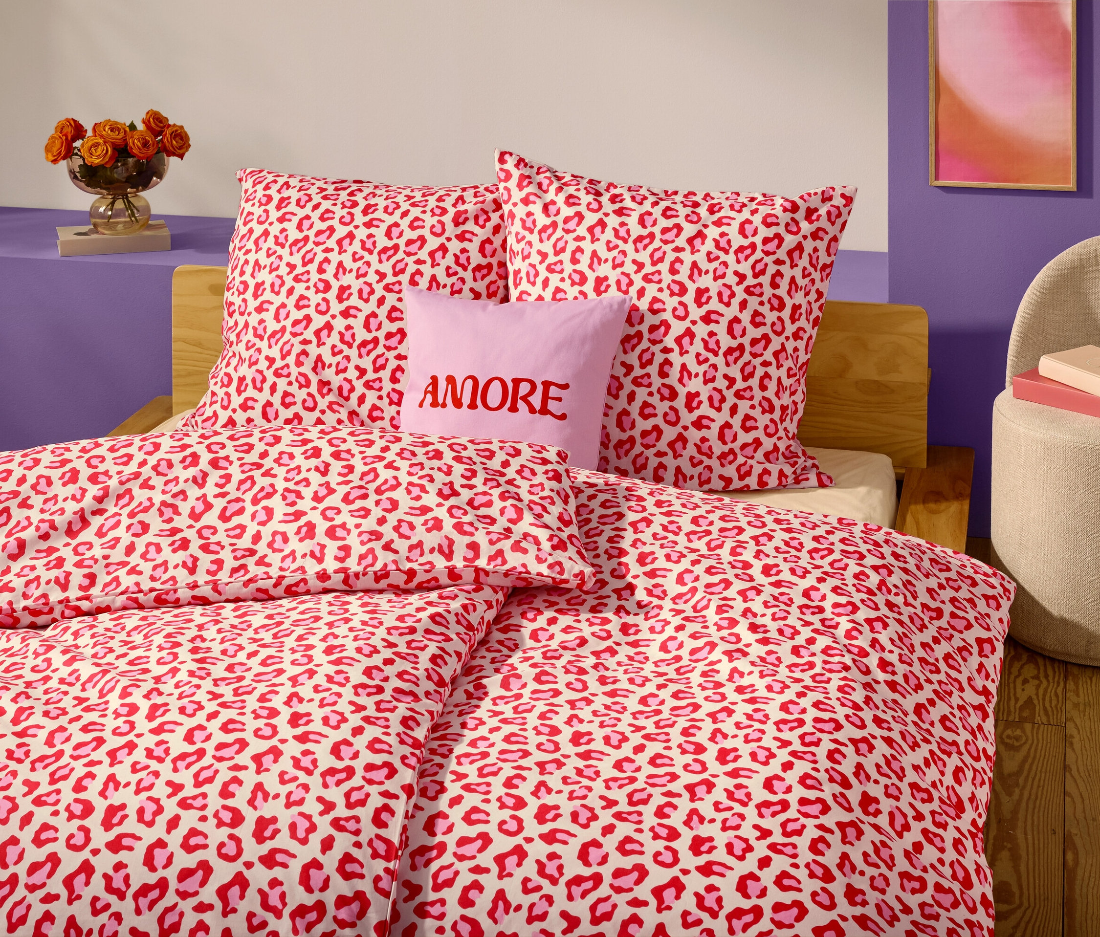 Na pierwszym planie łóżko z czerwoną i białą pościelą w panterkę i poduszkami. Lawendowa poduszka z napisem "AMORE" znajduje się przed dwiema poduszkami.