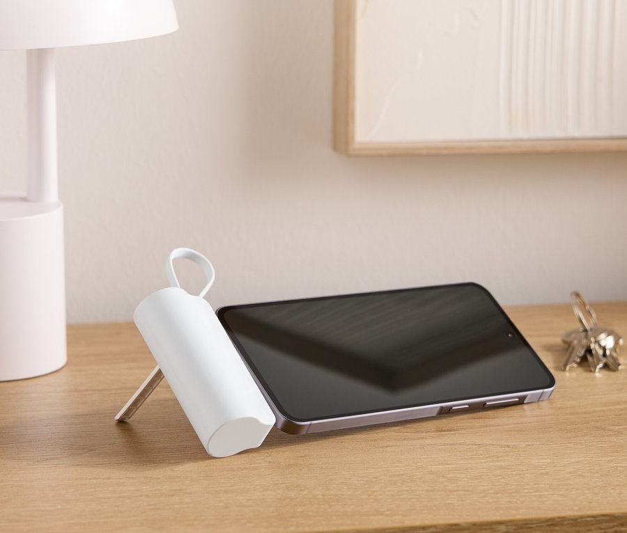 Na drewnianym stole stoi lampa, tablet, pęk kluczy i biały, cylindryczny przedmiot z uchwytem.