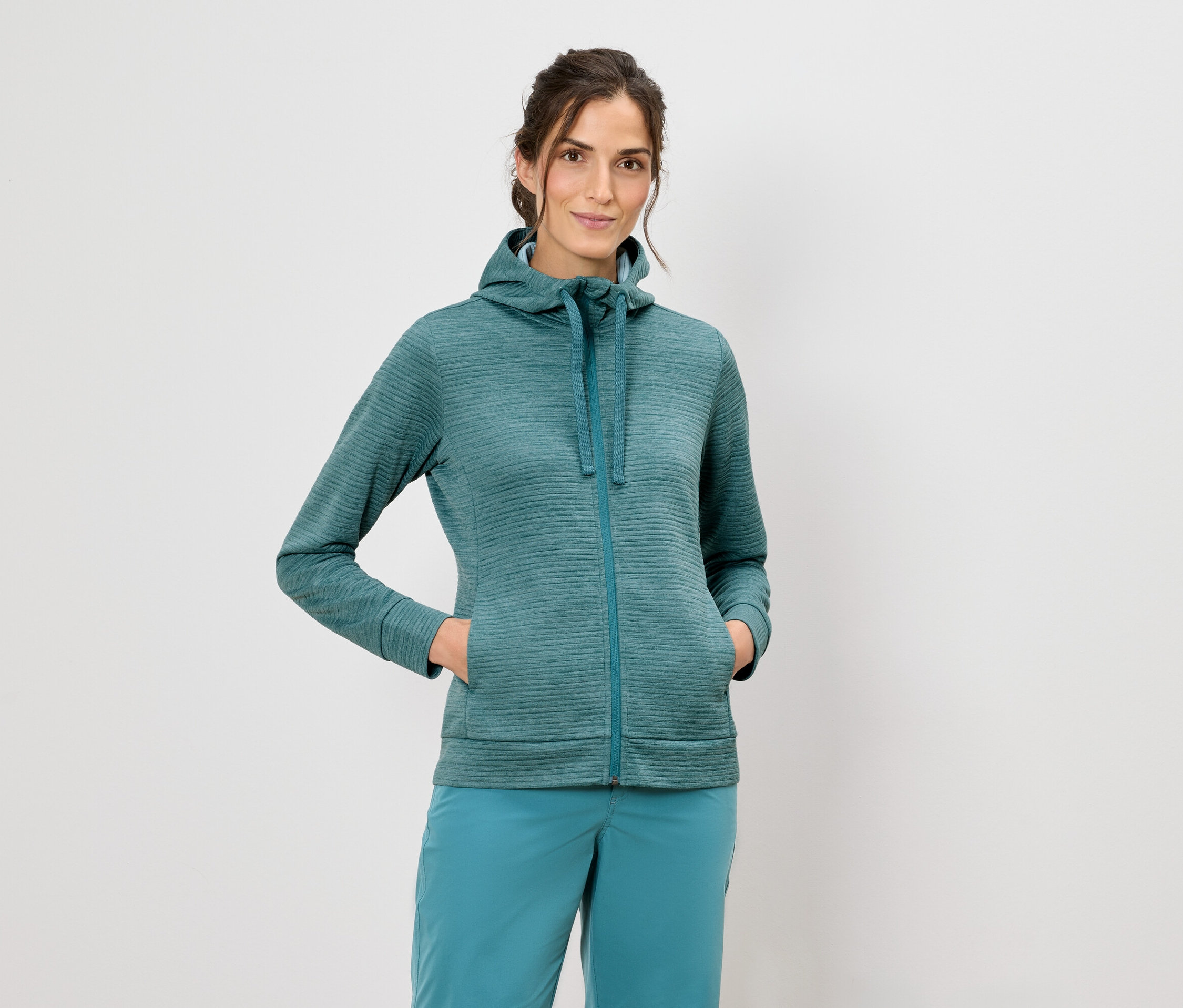 Kobieta w bluzie z kapturem i niebieskich spodniach stoi na białym tle.