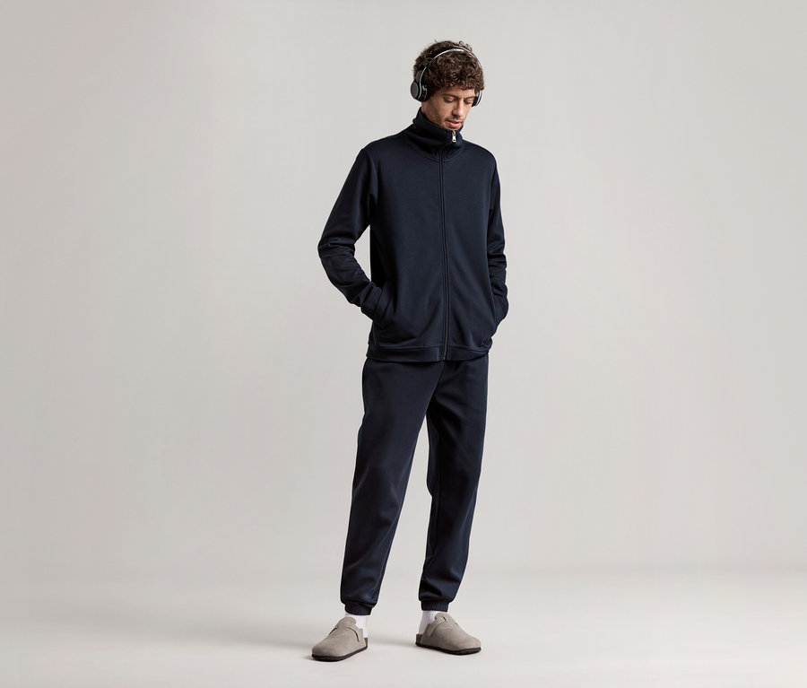 Mężczyzna w słuchawkach, ubrany w granatowy dres domowy.