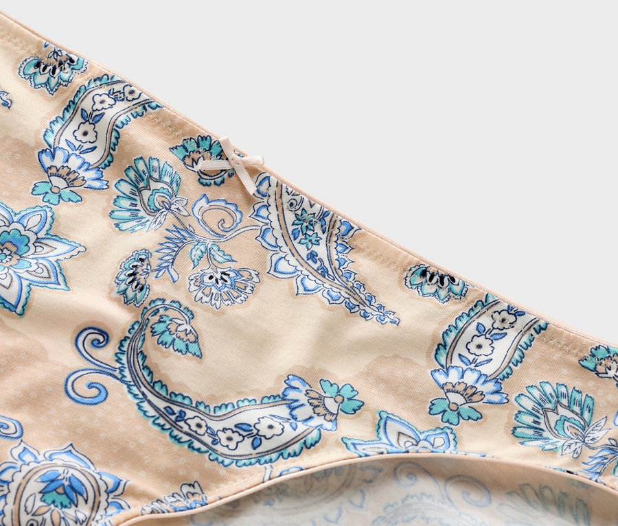 Zbliżenie beżowych majtek z niebieskim wzorem paisley i kokardką.
