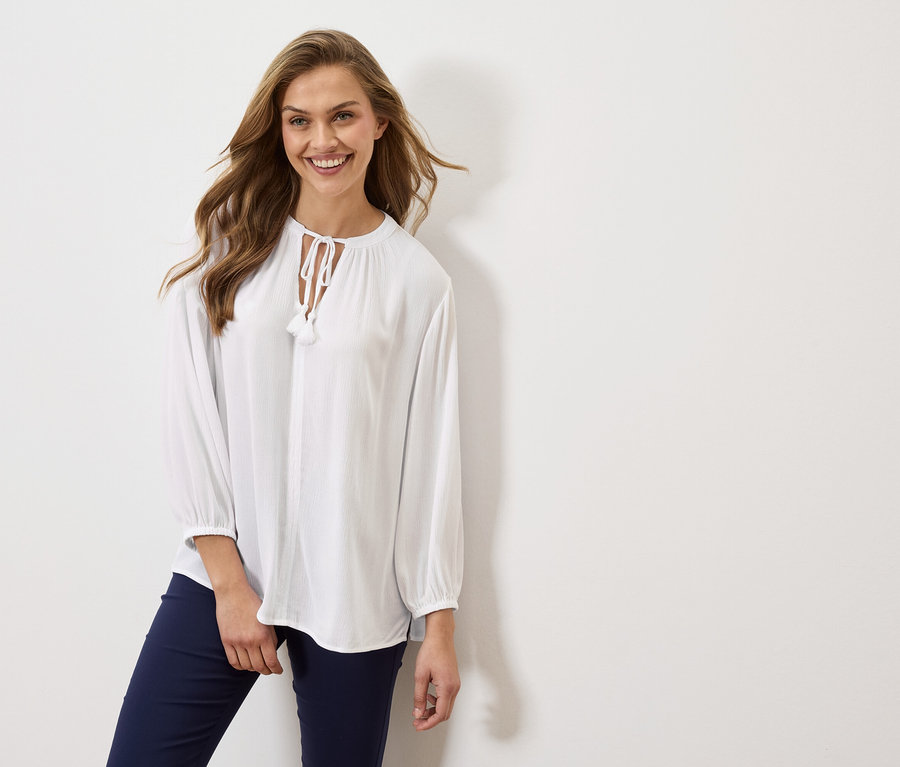 Kobieta ma na sobie białą bluzkę z długimi rękawami i granatowe spodnie.