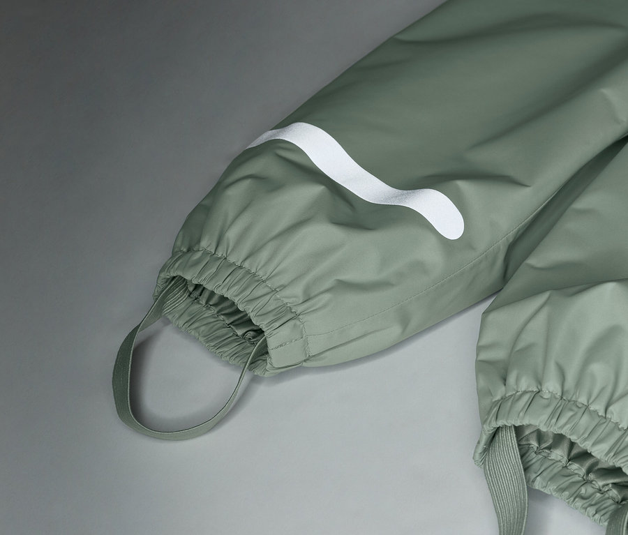 Zbliżenie na jasnozielone spodnie przeciwdeszczowe z białym logo i elastycznymi mankietami.