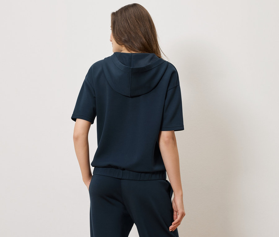 Widok z tyłu kobiety w granatowej bluzie z kapturem z krótkim rękawem i pasujących spodniach.