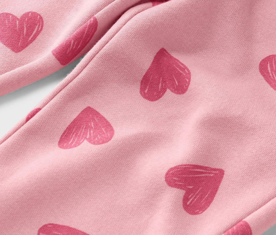 Zbliżenie jasnoróżowych spodni z różowymi nadrukami w kształcie serc.