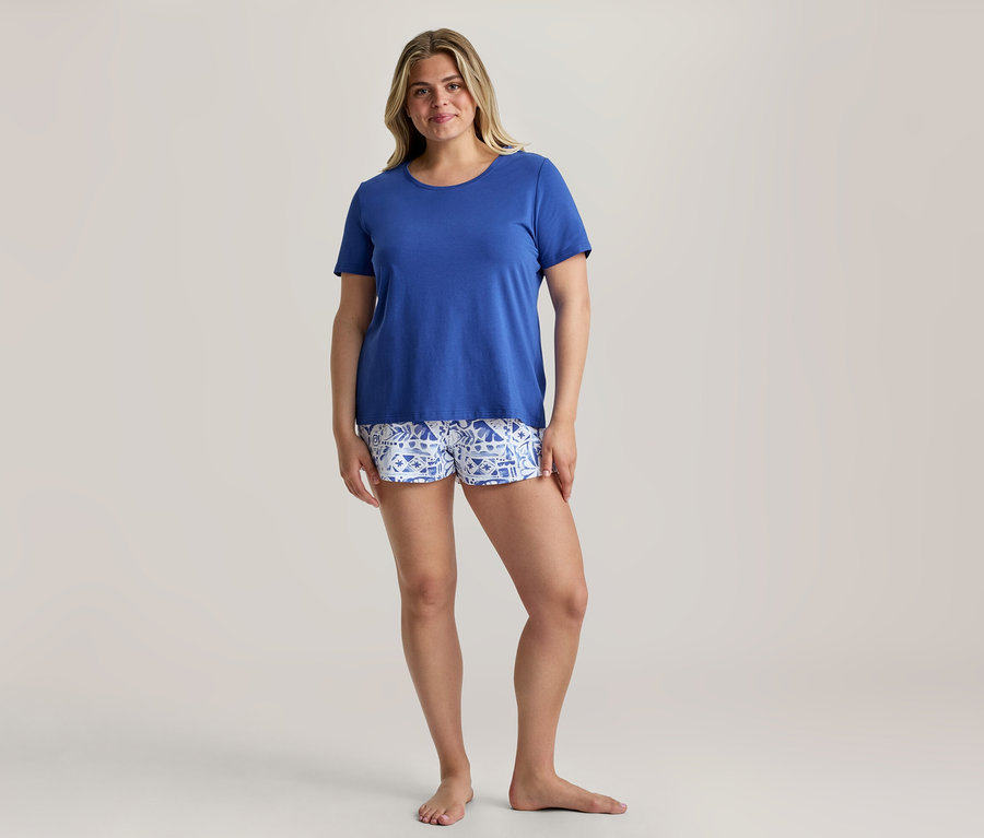 Uśmiechnięta kobieta w królewsko niebieskim T-shircie i wzorzystych szortach z zestawu piżamy shorty.