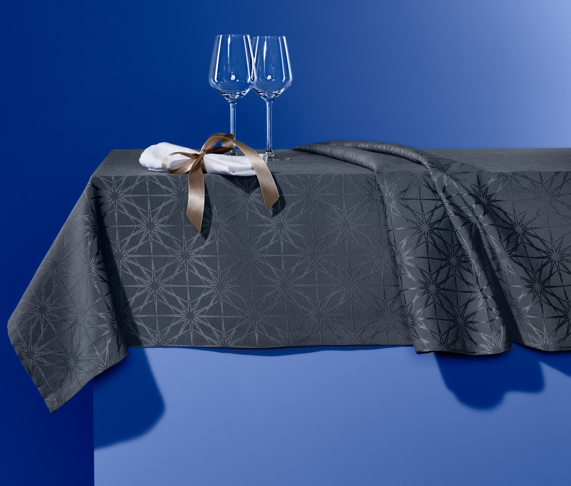 Dwa kieliszki do wina i serwetka z brązową wstążką stoją na obrusie żakardowym.