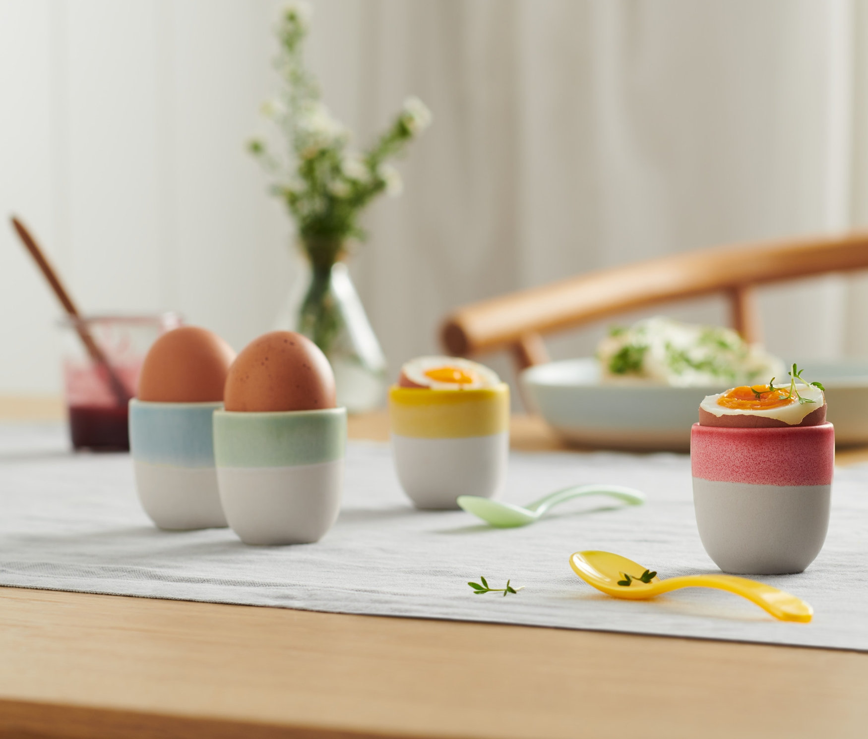 Cztery kieliszki do jajek z jajkami na stole.