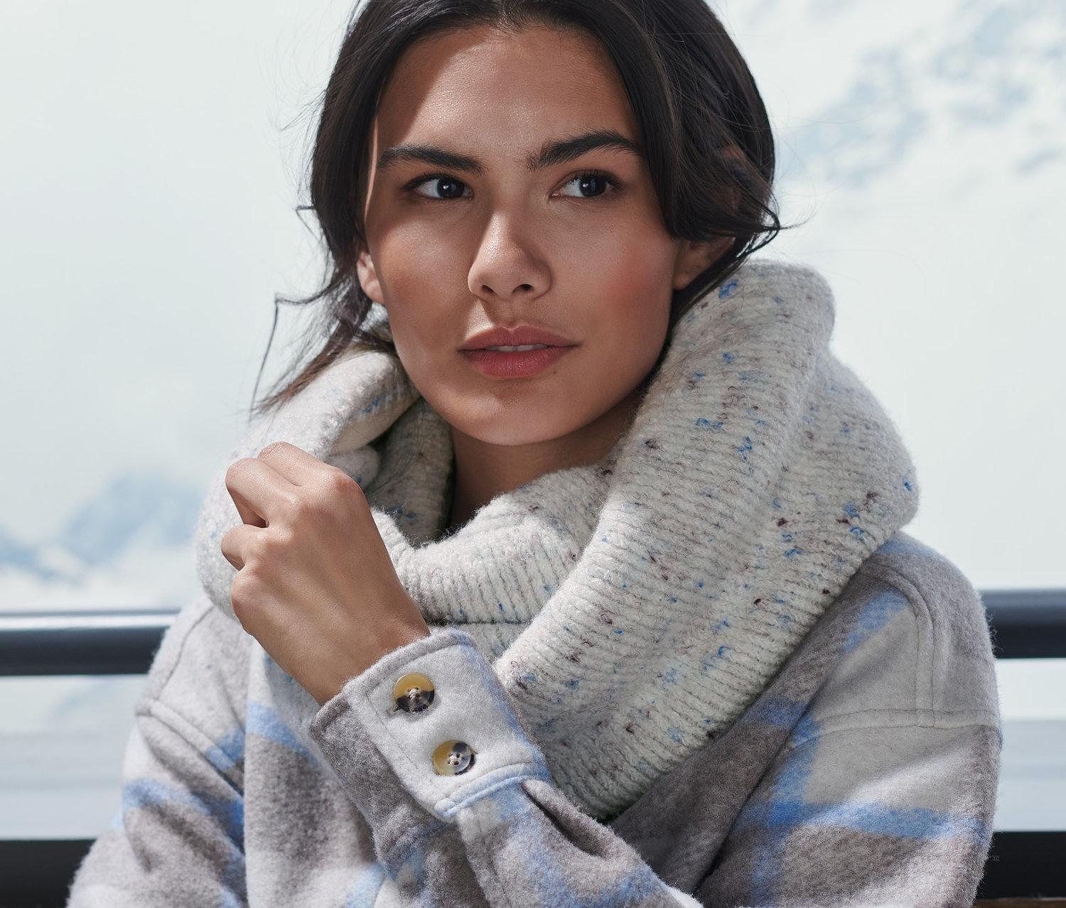 Kobieta siedzi na zewnątrz i ma na sobie szal-komin z dzianiny.